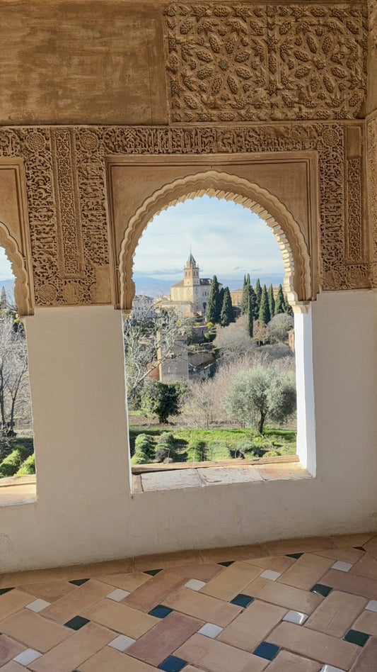 View through a carved arched window at the Alhambra, cypress trees and Granada beyond