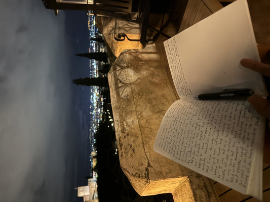 An open journal on a terrace at night, the Alhambra lit up above Granada
