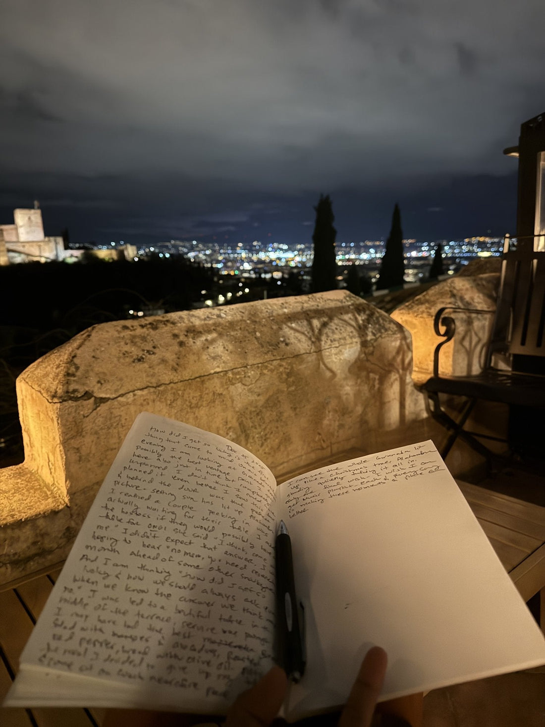 An open journal on a terrace at night, the Alhambra lit up above Granada