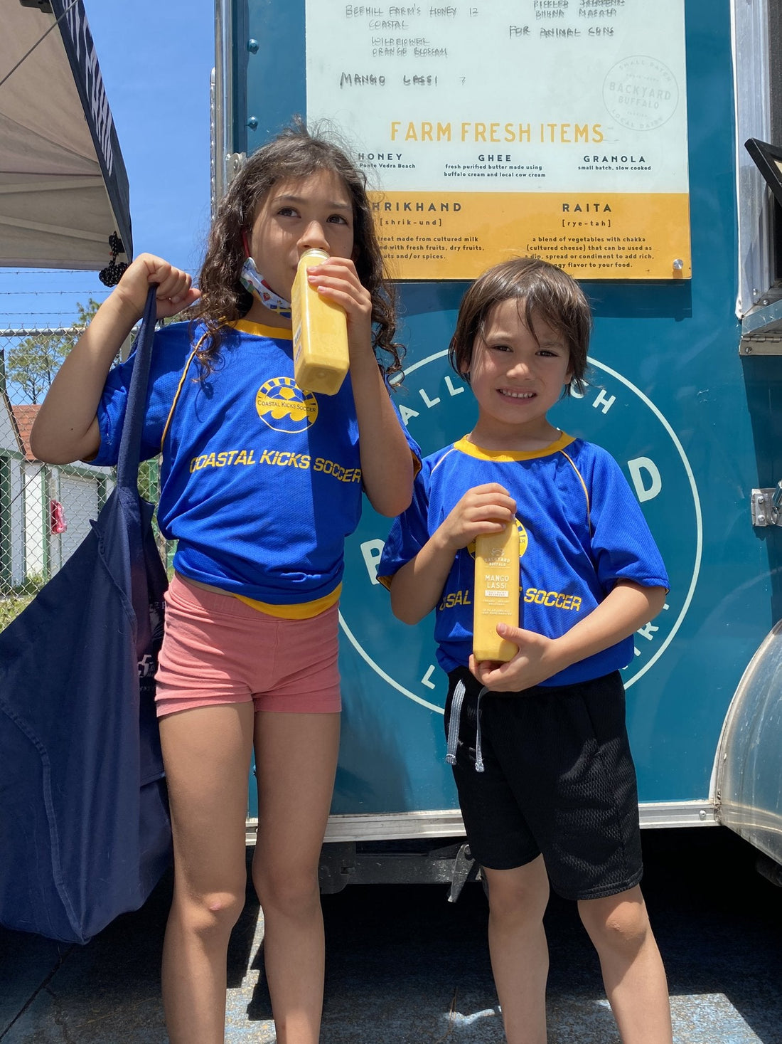 Two children drinking Backyard Buffalo mango lassi at the trailer