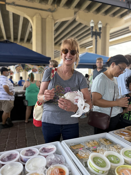 A customer holding a sample cup at the Backyard Buffalo table under the bridge at Riverside Arts Market