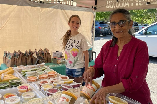 Two women at an outdoor market stall with food items on display.